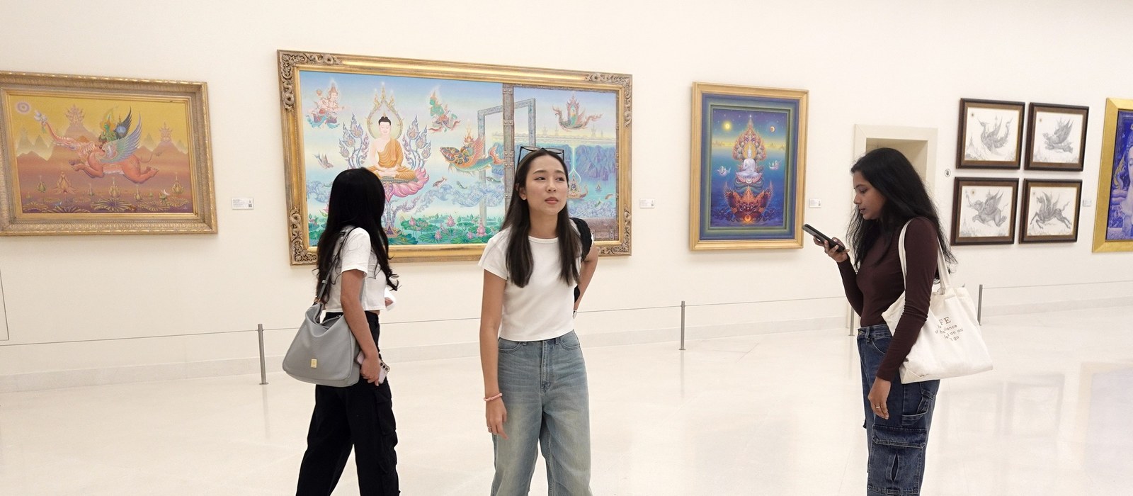 Three visitors in front of Buddhist paintings at MOCA — Bangkok museums on a cultural visit with a smartphone audio guide